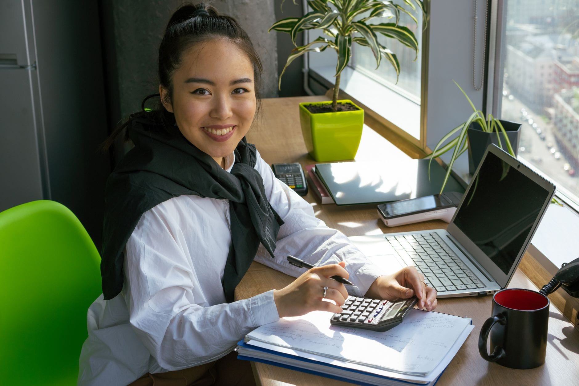 An accountant smiling at a sunny window desk with a calculator and notebook